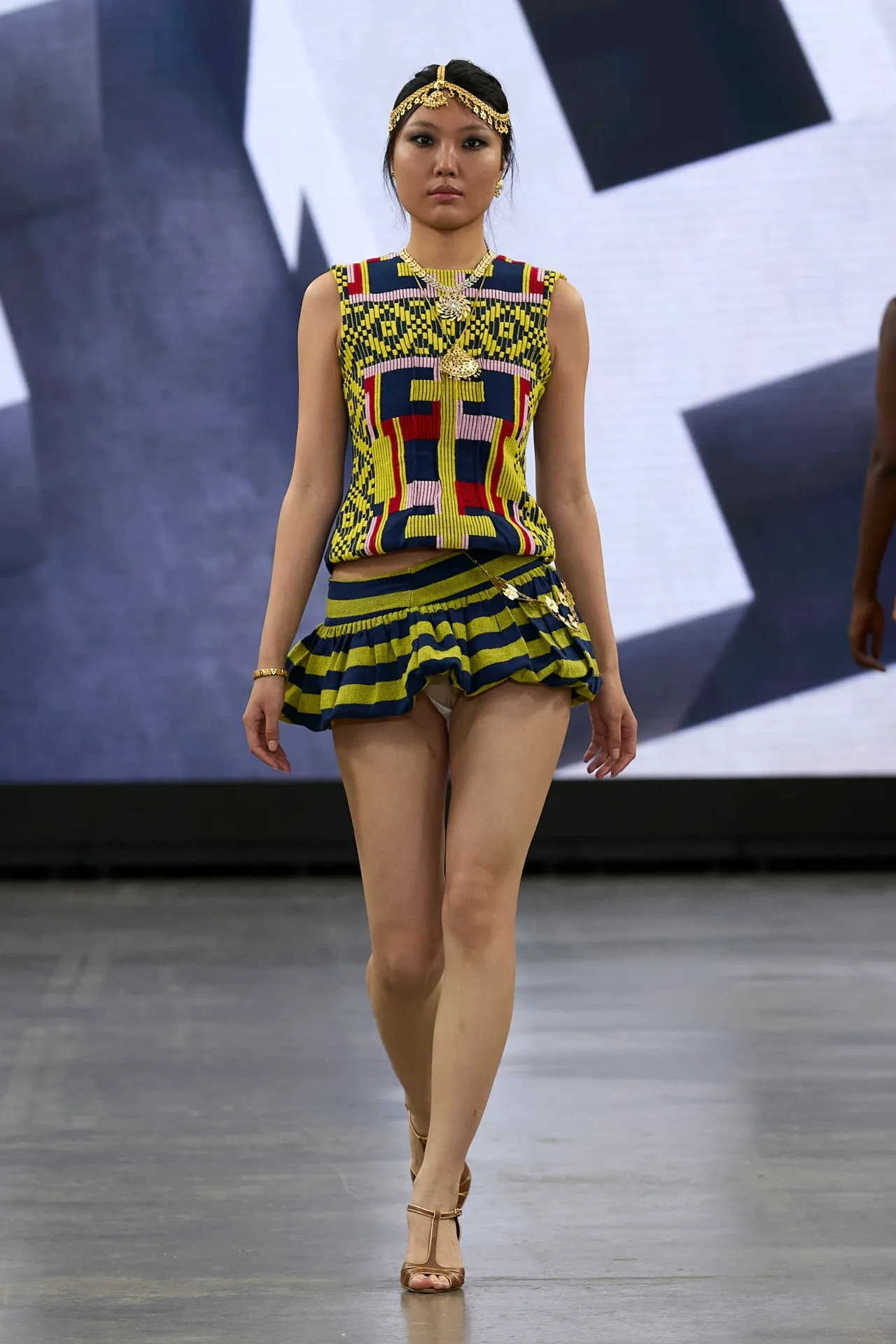 Runway photograph of a model in a vibrant handwoven top and ruffled skirt